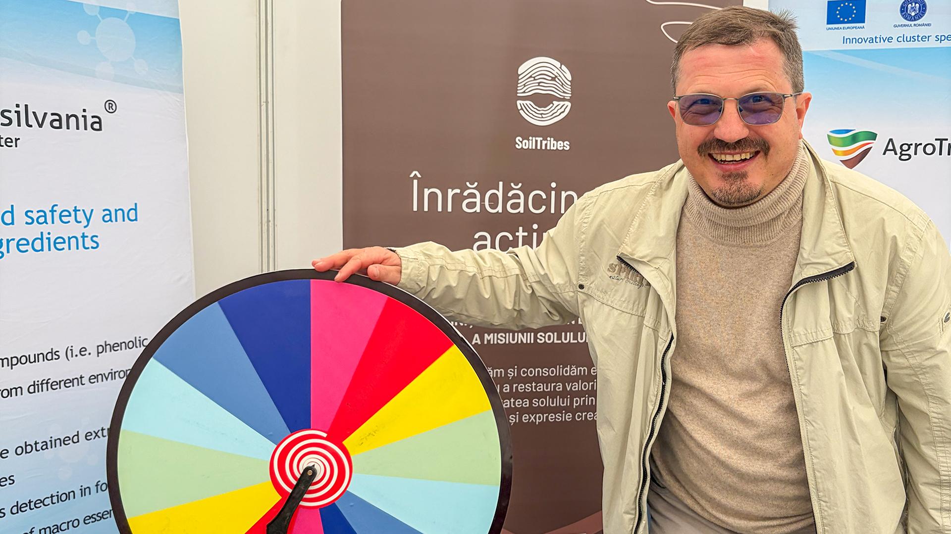 Person posing in front of SoilTribe stand at AGRARIA 2026, along with a spinning colorful wheel.