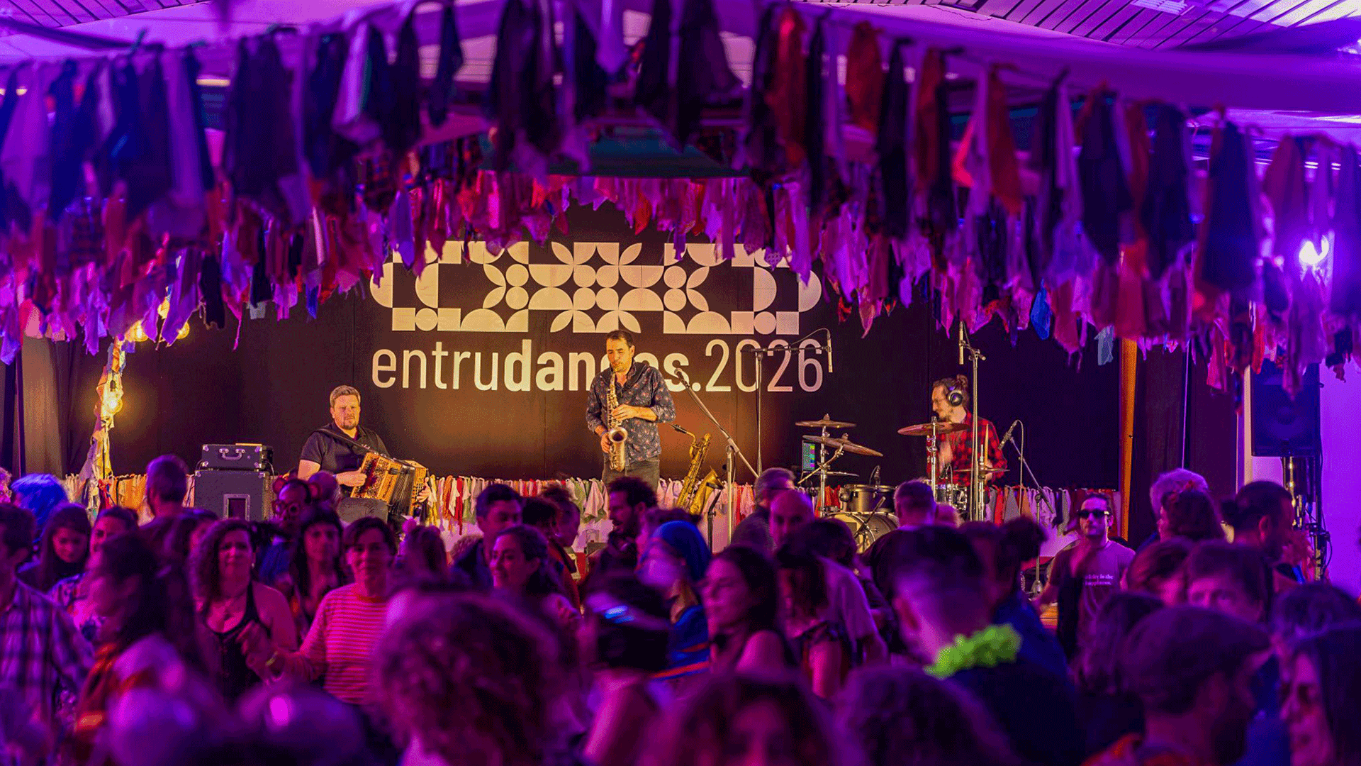 Crowd dances in front of a stage at Entrudanças 2026, where musicians perform under purple lighting and hanging decorations.